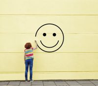 Girl drawing smiley face on to a wall